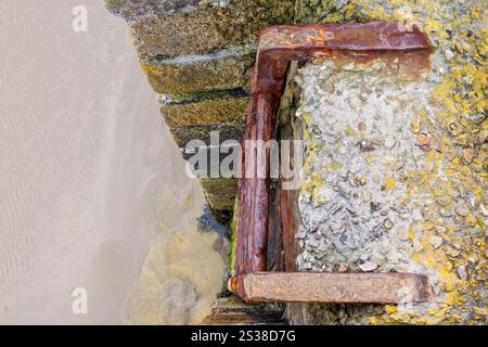 old rusty iron ladder down to the beach on a stone pier Stock Photo
