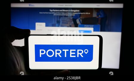 In this photo illustration, a person is holding a cellphone with the logo of Indian logistics company Porter (Porter.in) on screen in front of business webpage. Stock Photo