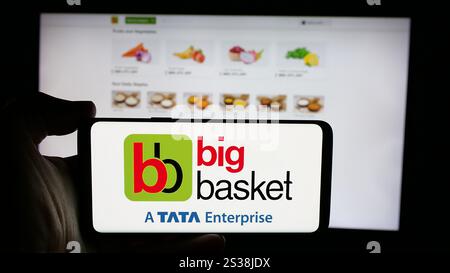 In this photo illustration, a person is holding a cellphone with the logo of Indian online grocery company BigBasket on screen in front of business webpage. Stock Photo