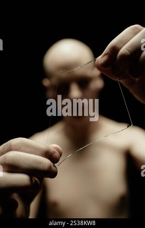 Close up on piece of broken glass in hands of unrecognizable man with deep shadows on face standing in dark studio against black background, blurred background, copy space Stock Photo