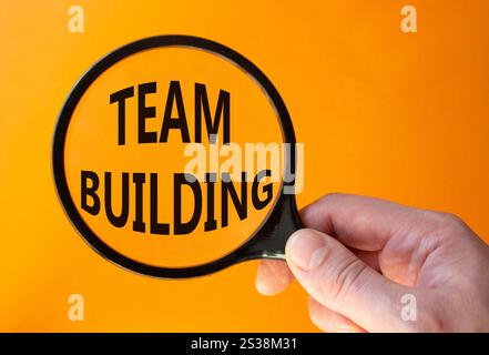 Team Building symbol. Concept word Team Building on magnifying glass. Businessman hand. Beautiful orange background. Business and Team Building concep Stock Photo