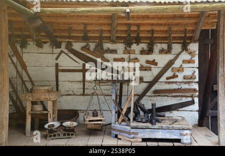 Collection of planers and retro wood saws hang on a wooden wall near an old house. Carpenters plane and other things on the wall. Collection of Stock Photo