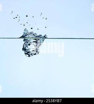 High-speed capture of a water droplet creating splash above and below water surface on a clear blue background. Crystal clear water splash isolated Stock Photo