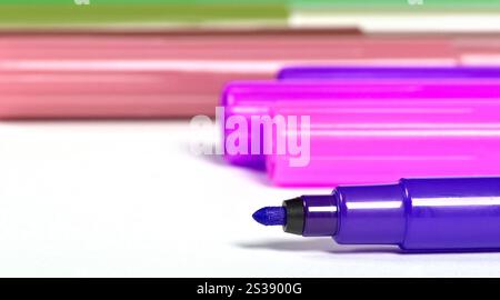 Close-up of a purple marker tip with blurred colorful markers in the background on a white surface. Vivid purple marker tip with assorted markers in Stock Photo