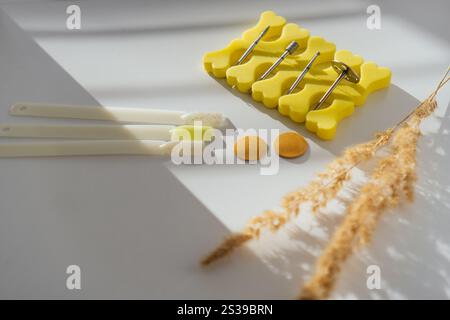 A set of nail art tools, including colorful polish samples, drill bits, and yellow separators, arranged creatively on a white background. Natural sunl Stock Photo