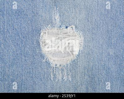 Close up view of light blue wash denim jeans ripped hole. Flat lay view, studio shot, lot of copy space. Stock Photo