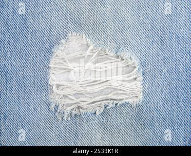 Close up view of light blue wash denim jeans ripped hole. Flat lay view, studio shot, lot of copy space. Stock Photo
