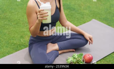 Sporty asian woman in sportswear drinking protein shake from bottle After Exercise for Energy Vitality in morning park sportswoman wellness health. Stock Photo