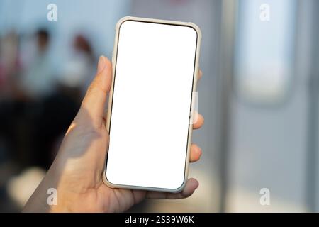 Mockup image of hand holding white mobile phone with blank screen in subway with many people in background. Stock Photo