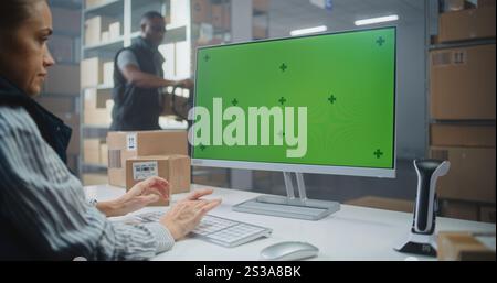 Distribution Center: Female Logistics Specialist Works on Computer in Warehouse Facility, Enters Data, Checks Inventory or Parcels Information. PC Screen Shows Green Screen Chroma Key. Dolly Shot. Stock Photo