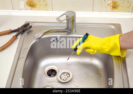 Close-up of handsome plumber repairing drain of kitchen sink. Photo of metalic sink and handyman with screwdriver. Close-up of handsome plumber hands Stock Photo