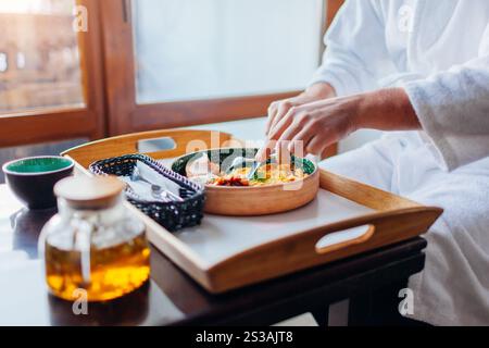 Close up of breakfast order in hotel room. Man eating eggs with toasts and drinking tea wearing white robe. Room service. Relaxing morning in resort o Stock Photo