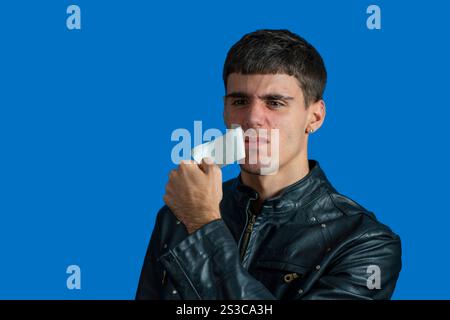 Young man removing a piece of adhesive tape from his face, expressing annoyance and discomfort Stock Photo