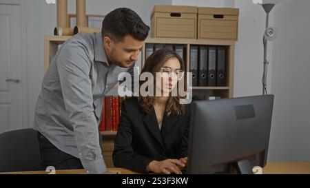 Man and woman working together at a computer in an office with shelves and folders in the background Stock Photo