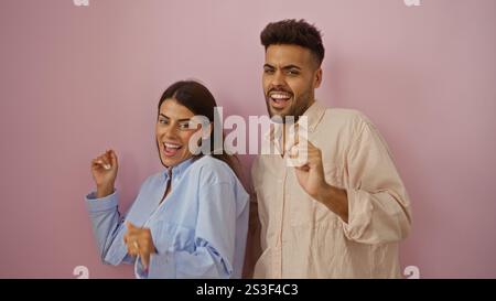 Man and woman dancing joyfully against a pink wall, expressing happiness and togetherness in a vibrant and isolated setting. Stock Photo