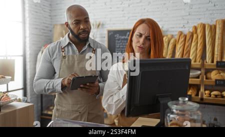 Man and woman in bakery shop working together with digital devices surrounded by bread and pastries on display Stock Photo