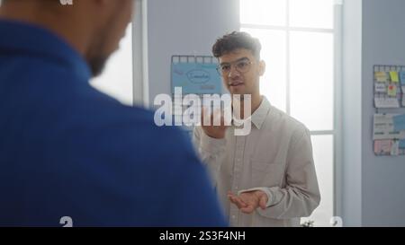Two men discussing business in an office room with one man gesturing while the other listens attentively Stock Photo