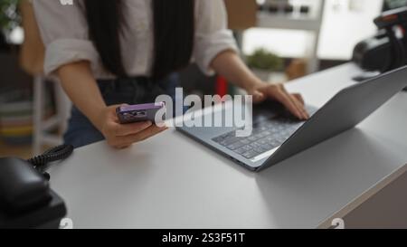 Young woman in a decoration store using a phone and laptop, focusing on her hands interacting with technology in an indoor, home decor setting. Stock Photo