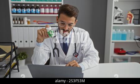 Young hispanic doctor in a clinic holding medication while conducting an online medical consultation using a laptop illustrating modern healthcare pra Stock Photo