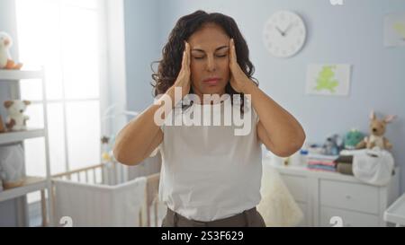 Woman with headache in bedroom holding head with hands, standing near cradle under clock in cozy room. Stock Photo