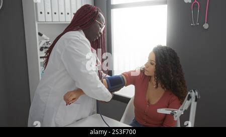 Woman patient having blood pressure checked by female doctor in clinic room with medical equipment visible indoors Stock Photo