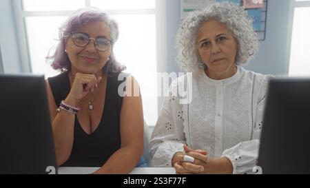 Women working together in an office with computers on a bright day, showcasing mature employees engaged in business activities indoors Stock Photo