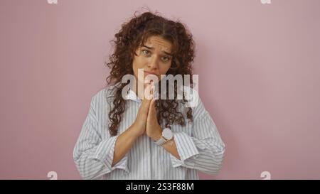 Young brunette hispanic woman in striped shirt with hands in praying gesture, looking at camera over isolated pink background Stock Photo