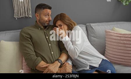 Couple watching a horror movie at home, woman covering her eyes in fear while man reacts on a cozy living room sofa Stock Photo