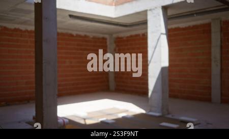 Defocused view of an unfinished construction site with brick walls and concrete pillars, illuminated by natural light filtering through an unfurnished Stock Photo