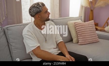 Handsome young muslim man with a beard sitting in a stylish indoor living room at home. Stock Photo