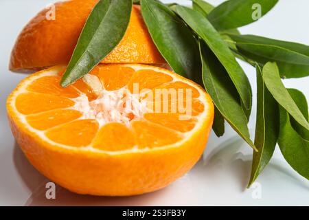 Cut fresh tangerine with green branch on white background. Close up. Stock Photo