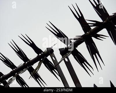 Sharp metal spikes line a commercial building rooftop, silhouetted against a gray sky. Stock Photo