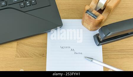 office desk and accessories, laptop, tape, stapler, paper with the tekst "Work at home" Stock Photo
