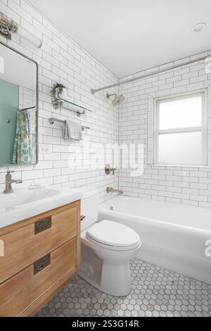 A bathroom with a natural wood floating cabinet, white marble countertop, marble hexagon tile flooring, and a subway tile shower. Stock Photo