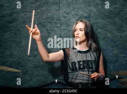 Female drummer practicing in small rehearsal studio, holding drumsticks, exuding passion, energy, creativity while performing.  Stock Photo