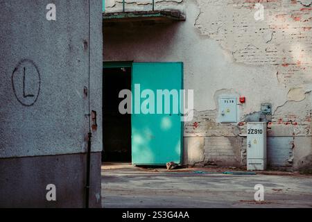 A teal door stands ajar in a weathered building.  The building's exterior is primarily light gray plaster with exposed brick and crumbling sections. Stock Photo