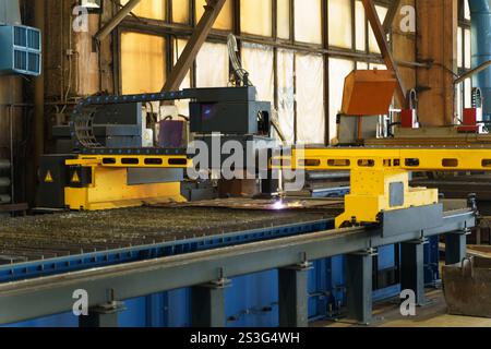 A large industrial machine expertly conducts laser cutting on metal sheets in an active workshop. Sparks fly as the precise technology shapes material Stock Photo