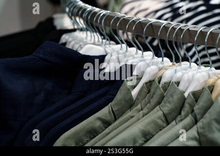 Rows of neatly arranged shirts in different colors hang on metal hangers, inviting shoppers to explore fabrics and styles within a modern retail space Stock Photo