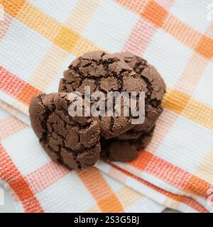 Freshly-baked chocolate crinkle cookies are displayed in a bright marble kitchen with orange and white accents. Stock Photo
