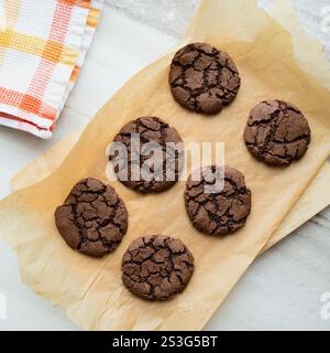 Freshly-baked chocolate crinkle cookies are displayed in a bright marble kitchen with orange and white accents. Stock Photo