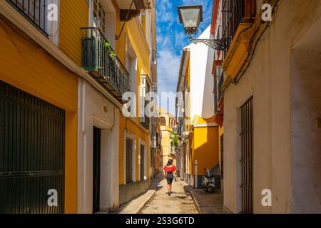 A Spanish woman walks down a narrow alley in the colorful old town of Barrio Santa Cruz in the Andalusian city of Seville, Spain. Stock Photo