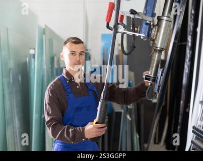 Male worker using control panel and lifting mechanism controls movement of window panes in an industrial workshop Stock Photo