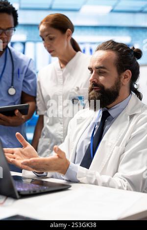 Professional doctor consulting with specialists in a meeting for research, collaborating in a hospital conference room. Medics reviewing patient histories and planning suitable treatment option. Stock Photo