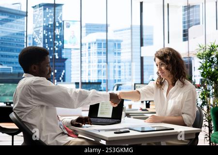 Recruiter hiring for newly opened company position, reaching agreement with applicant after validating his CV. HR specialist doing handshake with man after looking over his resume Stock Photo