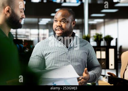 African american employee in company office checking progress on customer commissioned project. Man collaborating with colleague, comparing key data statistics after business audit Stock Photo