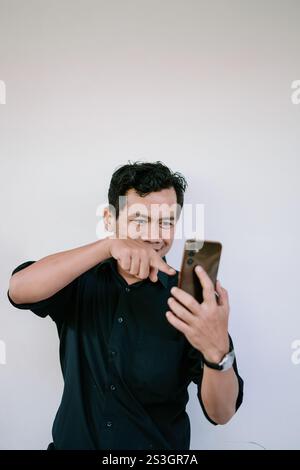 A man in a black shirt smiling while pointing at a smartphone screen, engaging with the device enthusiastically. Perfect for concepts like online comm Stock Photo