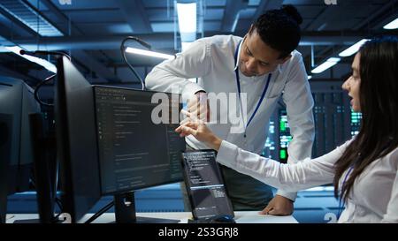 Team of admins in data center ensuring system can handle networking tasks. Teamworking colleagues in server room tracking network traffic with PC, making improvements, camera B Stock Photo