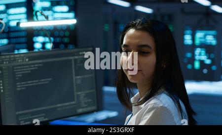Portrait of cheerful engineer in data center installing software on computer, troubleshooting issues. Smiling IT specialist in server room establishing performance benchmarks Stock Photo
