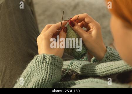 A detailed view of a young woman's hands carefully knitting with green yarn, using multiple needles. A cozy, focused moment of creativity captured up Stock Photo