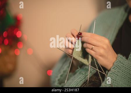 A detailed view of a young woman's hands carefully knitting with green yarn, using multiple needles. A cozy, focused moment of creativity captured up Stock Photo